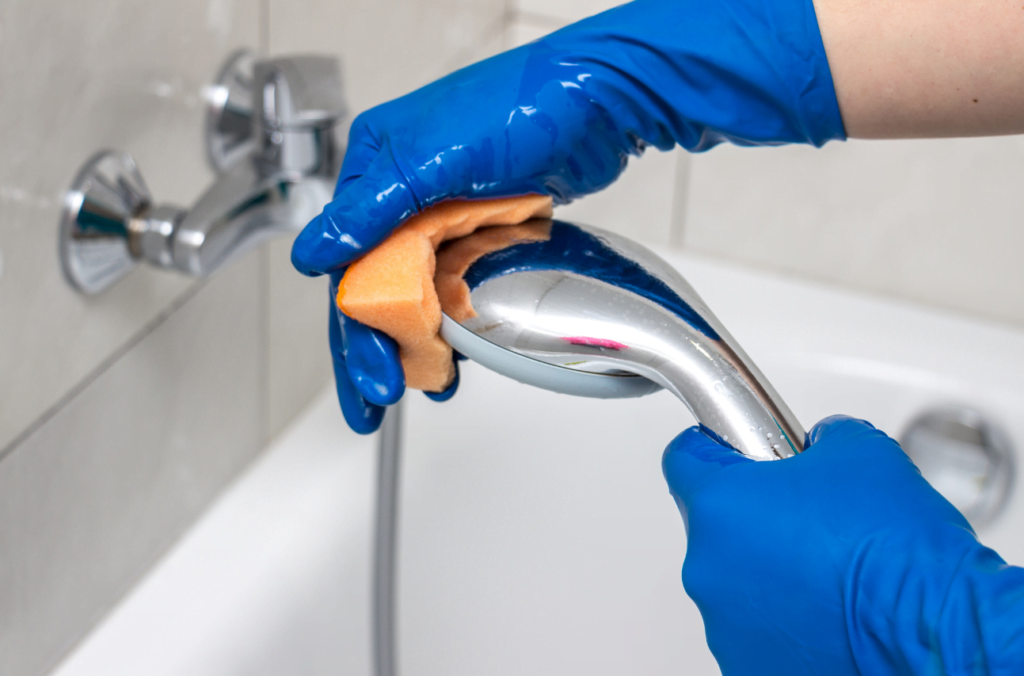 Avkalkning. Tvättar duschmunstycke med svamp och har blå handskar